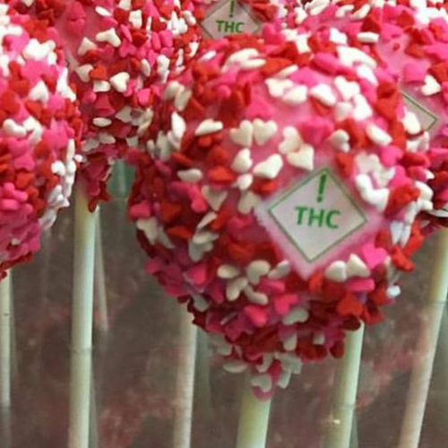 a white triangle with green ! THC symbol inside imprinted on a pink, red, and white cake pop