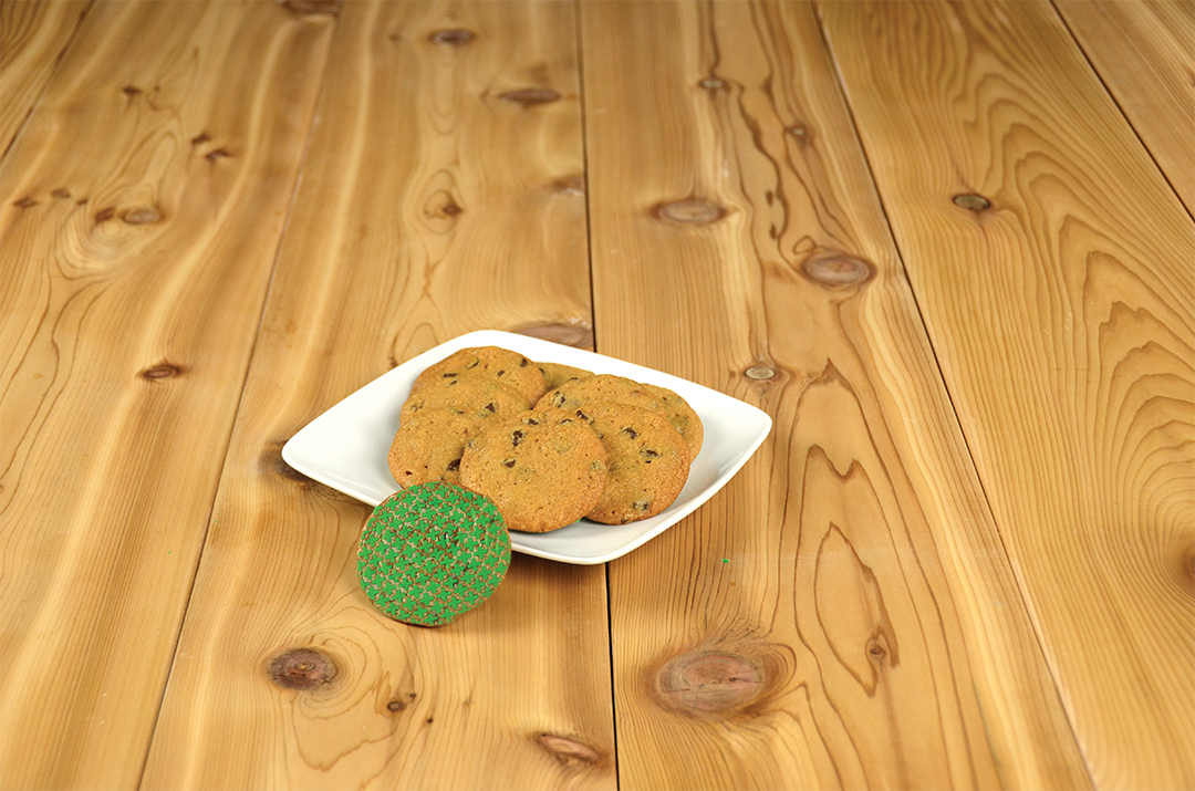 a tray of cookies with one flipped over displaying green cross symbols imprinted on it, on a wooden table