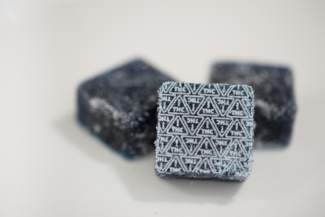 dark blue gummies with white THC ! triangle symbols imprinted on them