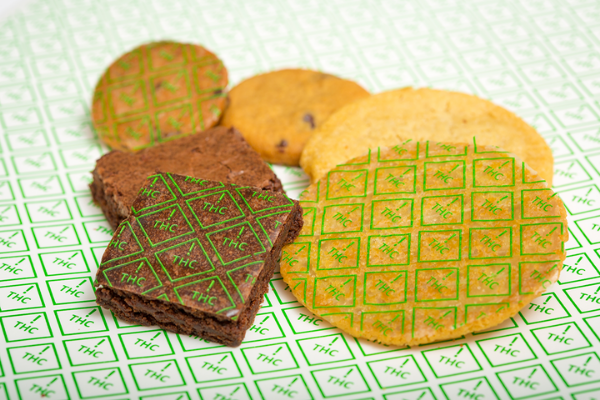 cookies and brownies with green diamond thc ! symbols imprinted on them laying on a baking sheet